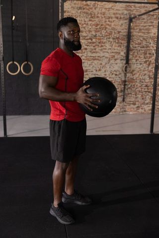 African american athlete holding heavy medicine ball in industrial gym wearing red shirt