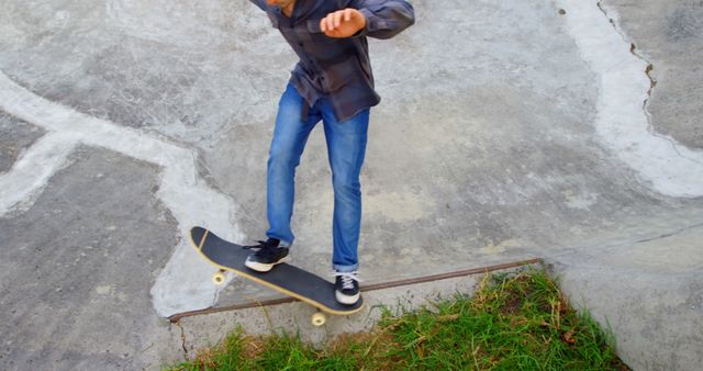 Teenage boy practicing skateboarding tricks at a concrete skatepark. Wearing a plaid shirt, jeans, and sneakers, he navigates a difficult section of the park. Ideal for use in promoting outdoor activities, action sports, urban lifestyles, and youth-related content.