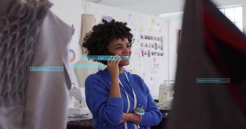 Fashion designer talking on phone in sewing studio with tape measure and moodboard