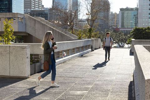 Urban commuters walking on sunlit concrete bridge woman talking on phone holding coffee