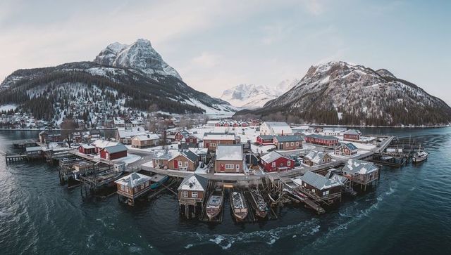 Stilt houses sitting along frozen fjord with fishing boats, piers and snow-capped peaks