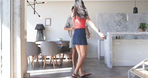 Couple stepping through sunlit sliding glass door into modern open-plan kitchen