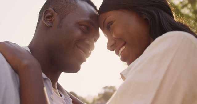 African American young couple sharing a tender moment, with warm sunlight enhancing the romantic atmosphere. Their close proximity and affectionate expressions convey a deep connection and love between them.