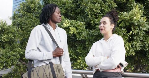Urban friends chatting on terrace with duffel bag beside greenery, casual conversation