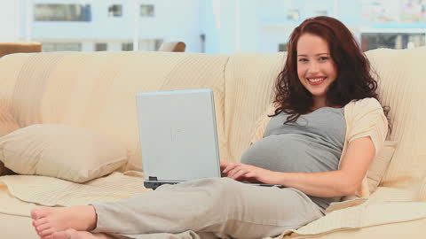 Pregnant Woman Smiling While Using Laptop at Home