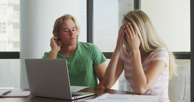 Couple sitting at home, deeply stressed while working on financial papers and using a laptop. Ideal for illustrating topics related to financial problems, money management, bills, budgeting, and family stress.
