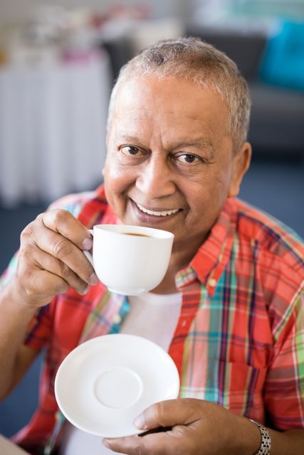 This image depicts a cheerful senior man enjoying a cup of coffee in a nursing home. His smile and relaxed demeanor convey a sense of contentment and well-being. This image can be used in marketing materials for senior living facilities, healthcare services, or retirement planning. It is also suitable for articles and blogs focused on elderly care, mental health, and lifestyle.