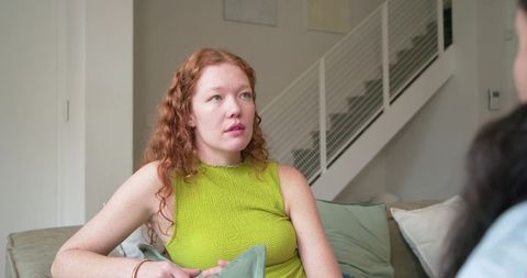 Redhead woman talking on couch holding cushion in modern cozy living room conversation