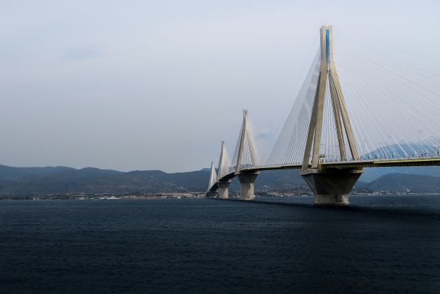Modern suspension bridge spanning calm sea with mountains in the background. Ideal for illustrating concepts of engineering marvels, architectural beauty, infrastructure, travel, and scenic views. Useful for travel brochures, engineering publications, infrastructure projects, and educational materials.