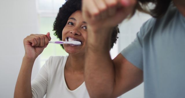 Happy couple brushing teeth together in morning, maintaining dental hygiene. Ideal for concepts related to daily routines, morning habits, relationship bonding, and healthcare advertisements. Picture highlights joy and partnership in everyday activities.