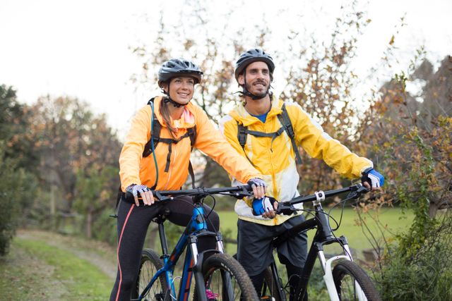 Couple enjoying a bike ride in the countryside, wearing helmets and outdoor gear. Ideal for promoting outdoor activities, healthy lifestyles, and adventure tourism. Perfect for use in advertisements, travel brochures, and fitness blogs.