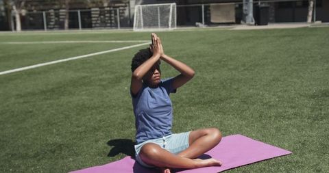 African american teen practicing yoga on purple mat at sunny soccer field for mindfulness