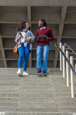 Multiracial university students walking down stairs holding tablet and smartphone talking
