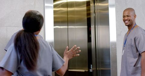 Smiling african american male nurse greeting colleague pointing to elevator in clinic