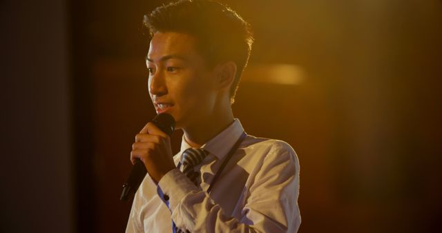 Young man confidently speaking while holding a microphone. Use for public speaking, professional presentations, business seminars, corporate events, and motivational speech visuals.