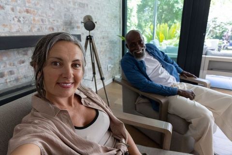 Mature couple smiling while taking selfie in modern brick lounge with garden view