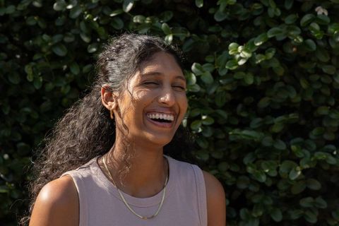 Sunlit african american woman laughing outdoors by green hedge, casual summer portrait