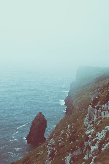 This image portrays a dramatic view of rocky outcrops along a misty coastline. The mist creates an otherworldly and serene atmosphere, ideal for designs focused on nature, tranquility, or coastal scenery. Perfect for background images, travel websites, inspirational posters, or serene-themed projects.