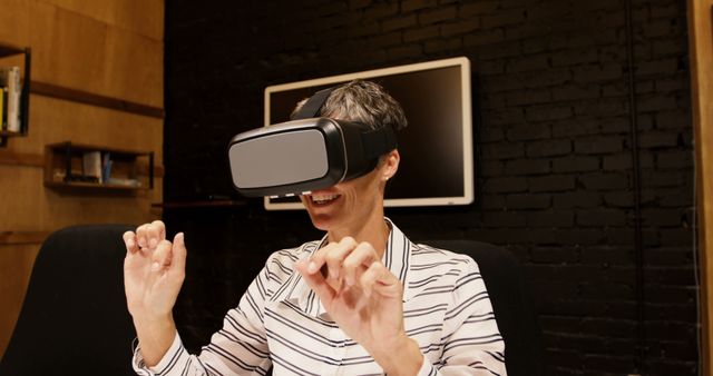 Smiling woman using VR headset in modern office setting with black brick wall. Ideal for tech websites, articles on virtual reality, cutting-edge technology demonstrations, workplace innovation, and business presentations. Highlights the use of modern technology in a professional environment.