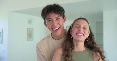 Diverse couple smiling and posing in minimalist pastel home for warm lifestyle portrait