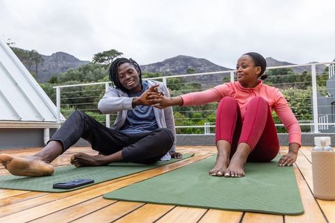 African american couple stretching and holding hands on rooftop yoga mats outdoor fitness