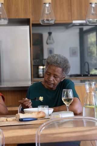 Senior african american woman eating at modern kitchen table with wine and bread