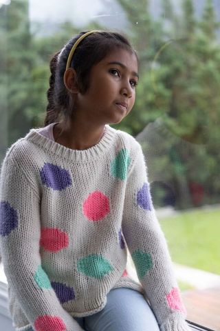 Contemplative asian girl gazing out window wearing pastel polka dot sweater and yellow headband