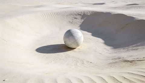 Resting marble sphere casting crisp shadow on sunlit sand dunes minimalist desert concept