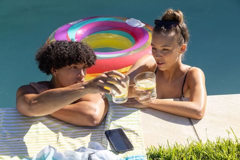 Young couple clinking lemon water glasses at backyard pool edge with colorful inflatable