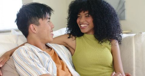 Laughing diverse couple sharing cozy moment on sofa, relaxed modern home romance