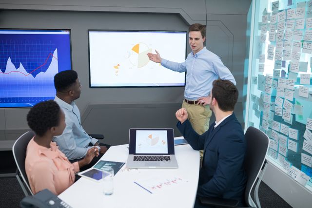 Executives are discussing graphs and data in a modern boardroom. A male executive is presenting information on a large screen while others listen and engage. This image is ideal for illustrating business meetings, corporate presentations, teamwork, and data analysis in a professional setting.