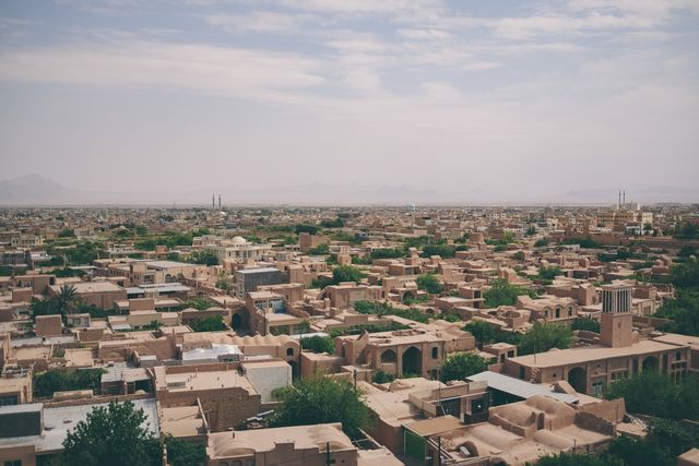 Historic cityscape showcasing traditional architecture in arid desert setting. Lush green trees intermingle with sunbaked buildings, creating a dynamic contrast. Ideal for travel blogs, historical articles, cultural studies, or architectural explorations.