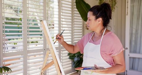 Woman Painting on Canvas in Sunlit Studio with Supplies