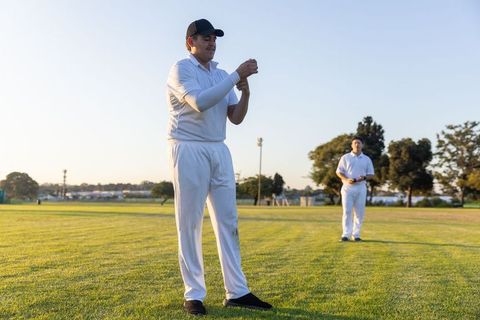 Cricket teammates adjusting ball on outfield during golden hour practice session