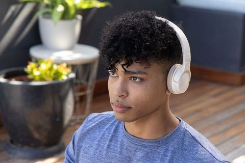 Contemplative african american man listening with white headphones on terrace