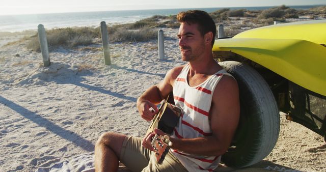 Young man sitting on sandy beach by car, playing guitar at sunset. Ideal for themes of travel, leisure, music, freedom, and outdoor activities. Perfect for summer vacation promotions and ads centered around relaxation and fun.
