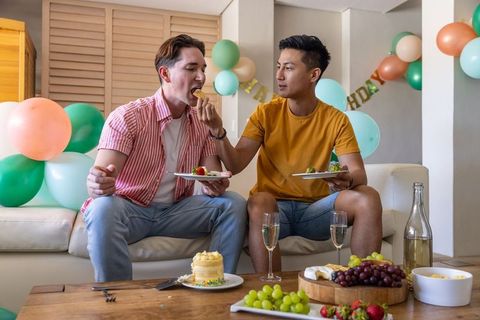Male couple sharing cake and toasting with champagne at intimate home birthday celebration