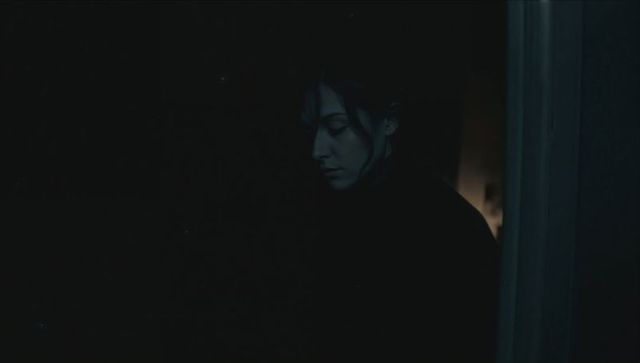 Moody asian woman standing in dim hallway gazing down by doorway lamp, low light