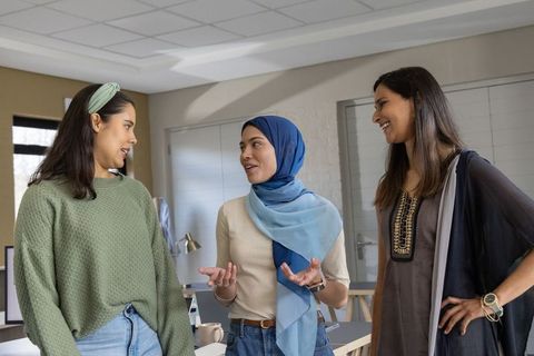 Diverse female colleagues collaborating, smiling and discussing ideas in modern office