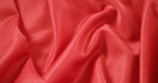 Close-up shot of vibrant red textile fabric with smooth texture and gentle folds, emphasizing material's softness and silky appearance. Excellent for backgrounds, fashion industry presentations, fabric industry catalogs, and creative design projects.