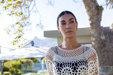 Elegant african american woman posing on sunlit modern terrace in white crochet top
