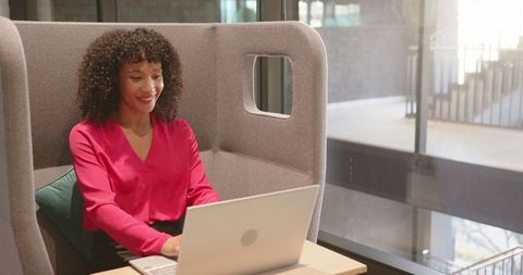 Smiling woman working remotely in modern office privacy booth