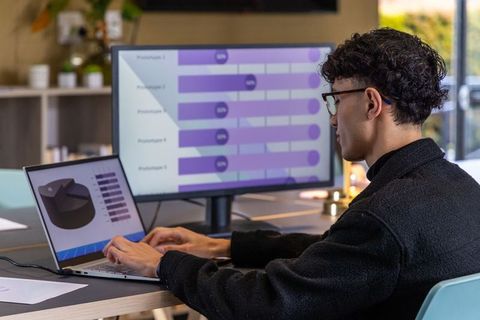 Young professional analyzing data on laptop and monitor with purple charts in workspace