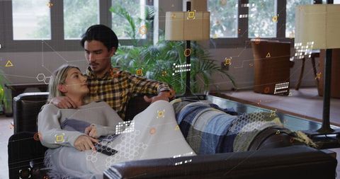 Young couple relaxing on leather sofa holding remote with augmented reality overlay