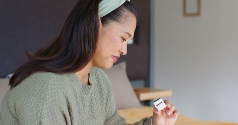 Mid-adult woman holding wireless earbuds in calming environment