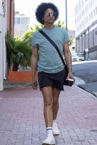 African american man walking on urban sidewalk wearing sunglasses holding coffee cup