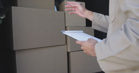 Warehouse Worker Inspecting Delivery Boxes with Clipboard