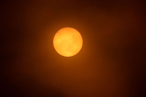Sun glowing through smoky orange sky during heavy haze creating dramatic warm atmosphere