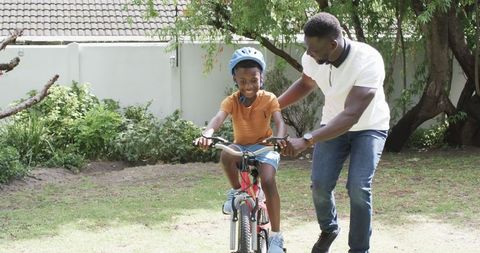 Father Teaching Son to Ride a Bike in Sunny Backyard