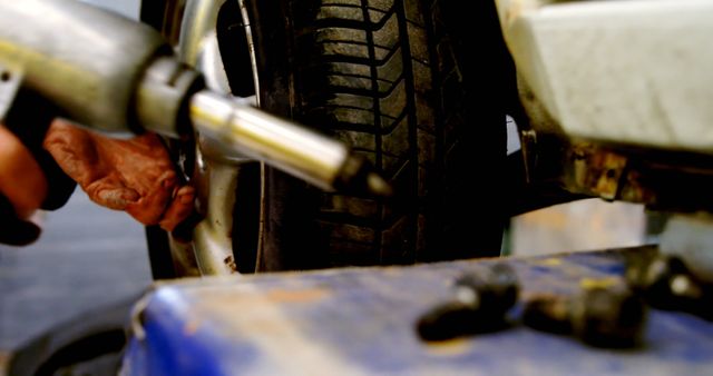 Mechanic focusing on tightening the wheel of a vehicle using a power tool in an auto repair shop. Ideal for illustrating concepts related to motor vehicle maintenance, mechanical work, and services provided at auto shops or garages.